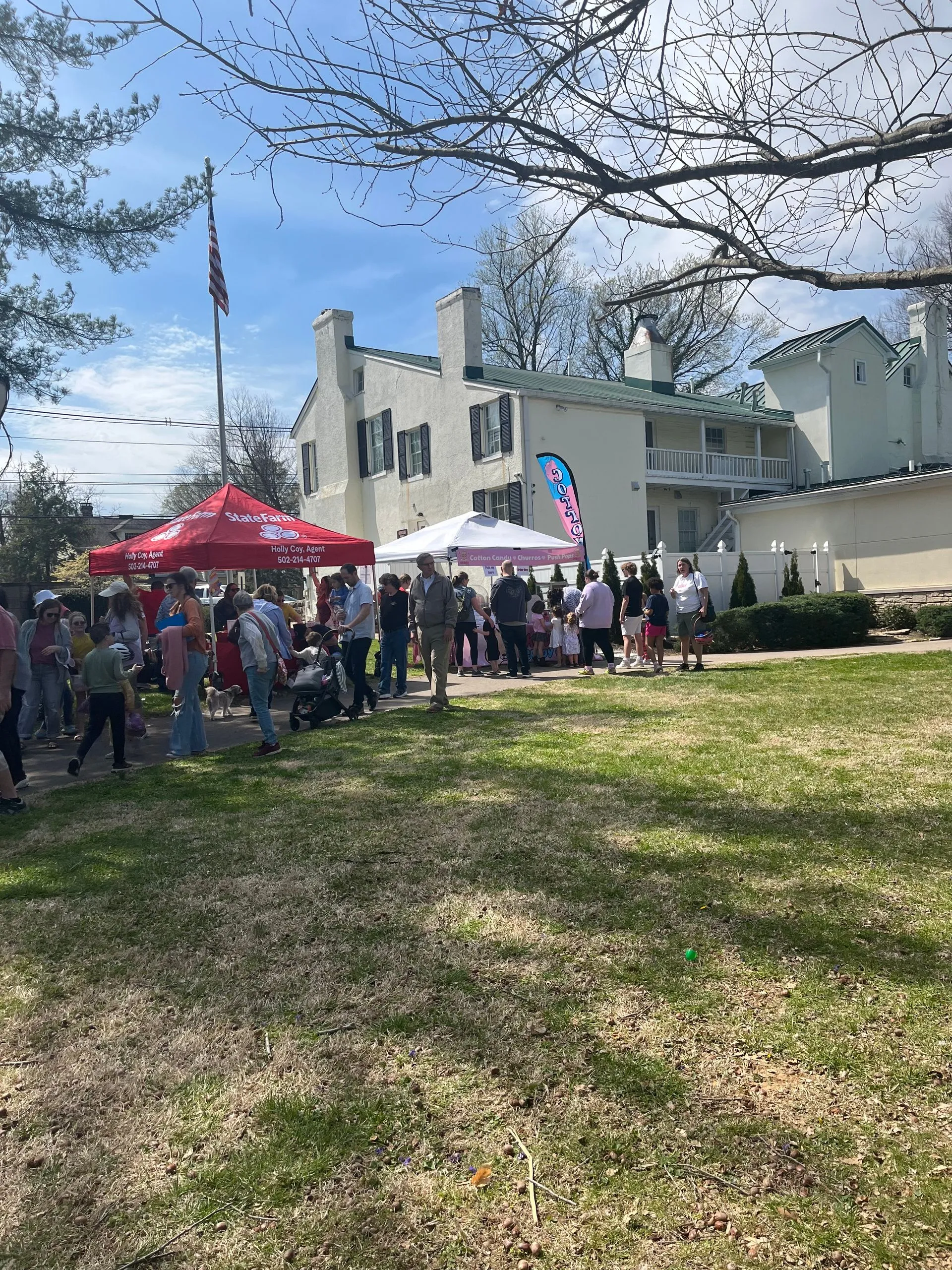 Crowd lines at vendor tents outside white building with flag.